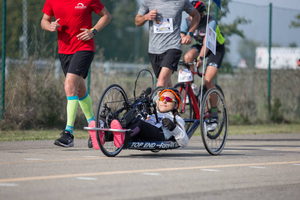 atleta discapacitada que entrena con su bicicleta de mano con ciclistas y corredores a su lado - physical impairment athlete sports race wheelchair fotografías e imágenes de stock