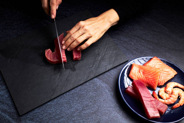 cuoca donna che prepara alcuni pezzi di tonno rosso e salmone per preparare sushi su una lavagna. concetto di cibo asiatico - prepared tuna foto e immagini stock