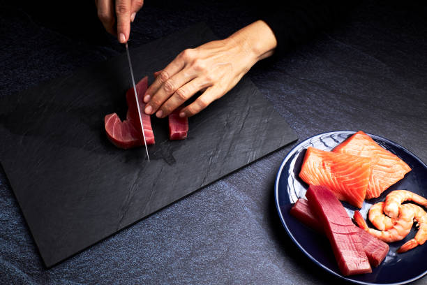 Female cook preparing some pieces of bluefin tuna and salmon to make sushi on a blackboard. Asian food concept stock photo