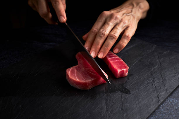 Female cook preparing a piece of bluefin tuna to make sushi on a blackboard. Asian food concept Female cook preparing a piece of bluefin tuna to make sushi on a blackboard. Asian food concept artisanal food and drink photos stock pictures, royalty-free photos & images