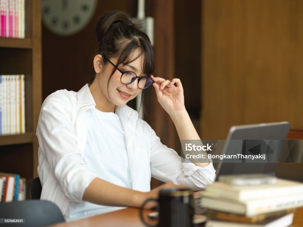 Side view of female student doing homework on digital tablet in cafe Side view of female student with eyeglasses doing homework on digital tablet in cafe Dissertation Stock Photo