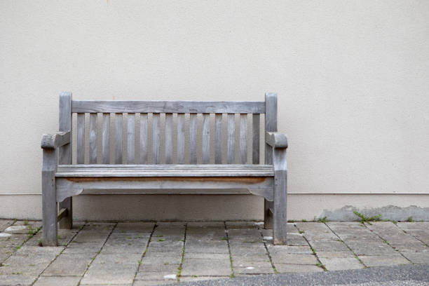 Outdoor wooden bench with white wall background.