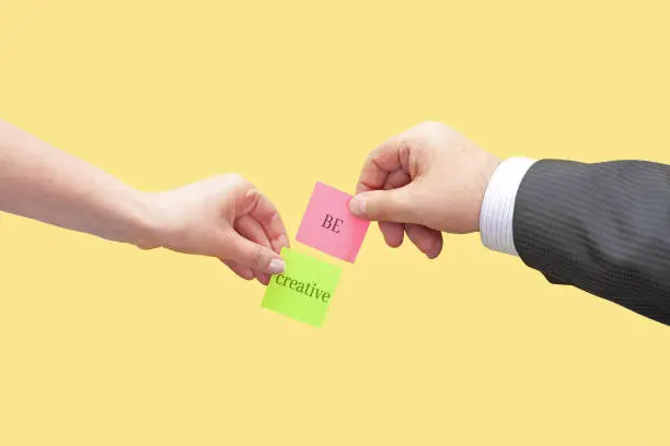 Two hands hold two sticky notes with the words Be Creative. Conceptual image of basic concepts for creativity.