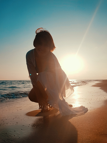 Young woman in white cover up dancing on the beach on  sunset