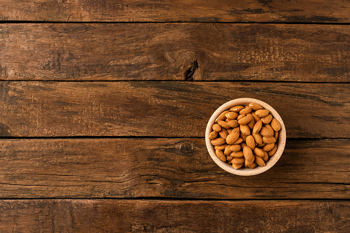Tasty almonds in bowl on wooden background with copyspace. Top view