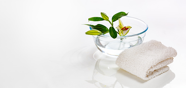 a flower and a lily bud in a transparent glass vase and a white towel. Spa concept.