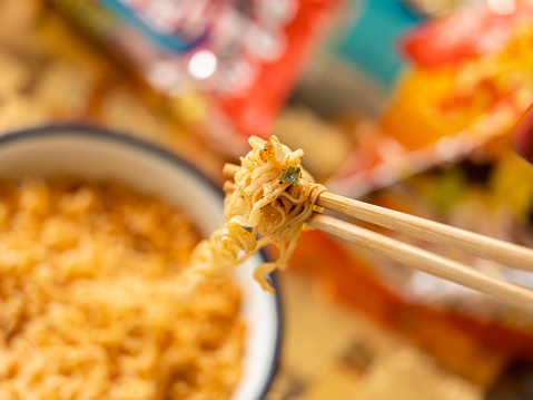 The most popular Asian fast food, available internationally, here a mouthful of freshly prepared instant noodles are on chopsticks, ready to be eaten. Shallow depth of field with the focus being on the noodles at the end of the bamboo disposable chopsticks.