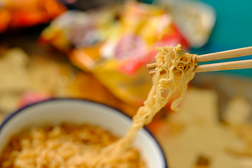 The most popular Asian fast food, available internationally, here a mouthful of freshly prepared instant noodles are on chopsticks, ready to be eaten. Shallow depth of field with the focus being on the noodles at the end of the bamboo disposable chopsticks.