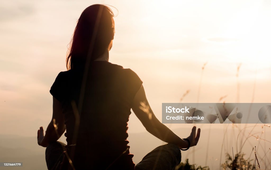 Silhouette of young woman practicing yoga outdoors Meditating Stock Photo