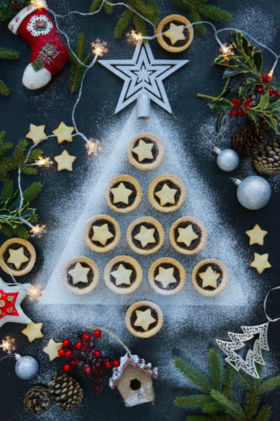 istock Image mince pies laid out like Christmas tree surrounded by decorations, festive dessert, crispy pastry with sweet mincemeat (mixture chopped dried fruit, distilled spirits, spices), topped with star shaped pastry sprinkled with icing sugar, elevated view 1321665651