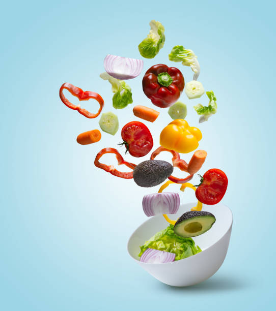 istock Sliced vegetables falling into bowl with salad on blue background 1321666036