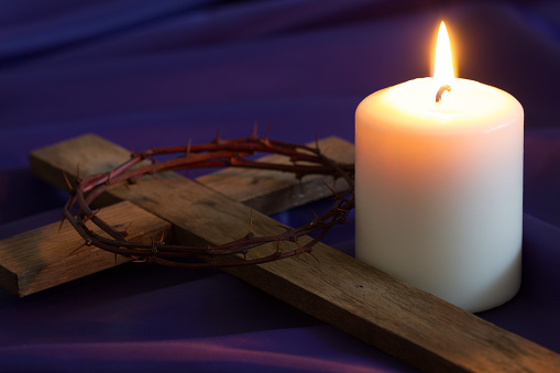 Candle and wooden cross with thorns on violet fabric background. Lent and prayer concept