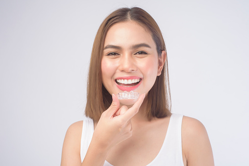 A young smiling woman holding invisalign braces over white background studio, dental healthcare and Orthodontic concept.