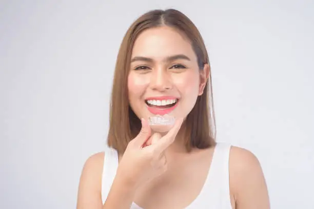 A young smiling woman holding invisalign braces over white background studio, dental healthcare and Orthodontic concept.