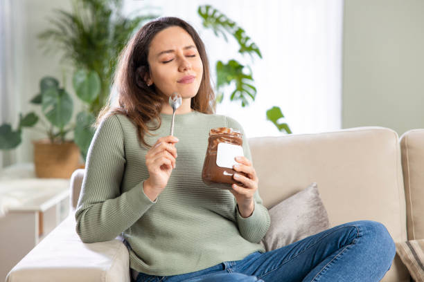 istock Young woman eating chocolate from a jar while sitting on on a couch 1321676204