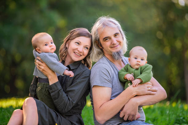 自然の中で休んでいる2人の小さな双子を持つ幸せな夫婦。緑の背景に対する肖像画 - senior adult family cheerful couple ストックフォトと画像