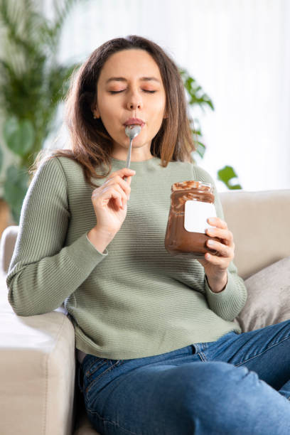 Young woman eating chocolate from a jar while sitting on on a couch