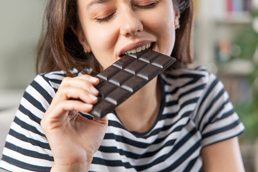 Young woman eating chocolate bar in living room