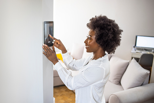 Young african girl woman lady adjusting remote climate control panel settings wall touch screen set heating conditioning switch on security system energy saving mode, black lady use smart home concept.