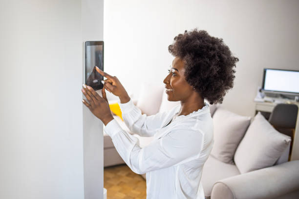 Young african girl woman lady adjusting remote climate control panel settings wall touch screen set heating conditioning switch on security system energy saving mode Young african girl woman lady adjusting remote climate control panel settings wall touch screen set heating conditioning switch on security system energy saving mode, black lady use smart home concept. smart thermostat stock pictures, royalty-free photos & images
