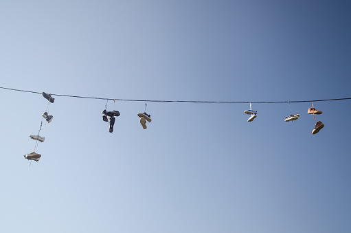Old Shoes hanging on electrical wire against a sky.