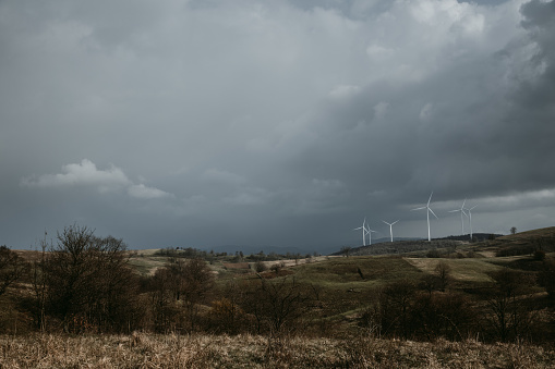 Farm of wind turbines for renewable wind energy on far horizon on hills of Romania under the dark cloudy sky. Copy space.