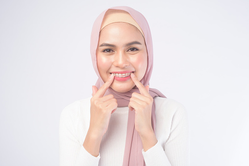 A young muslim woman holding colorful retainer for teeth over white background studio, dental healthcare and Orthodontic concept.