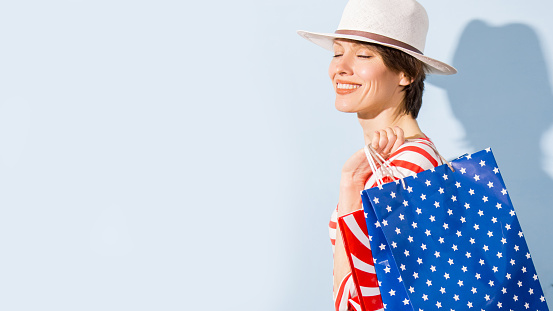 Beautiful woman holding shopping bags stars, stripes in white, blue, red colors over light blue background