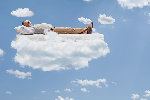 Mature man lying on a of mattress and floating on clouds