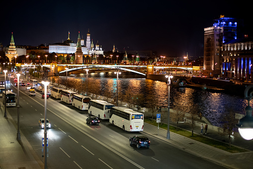 Moscow by night, multiple lane street with cars and tour buses, street lights, bridge over Moscva river, illuminated Kremlin in the background