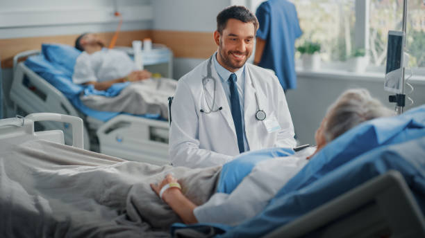 hospital ward: friendly doctor talks to beautiful senior female patient resting in bed, explains test results, gives recovery advice. arzt spricht mit alter dame, die sich nach erfolgreicher operation erholt - hospital patient bed doctor stock-fotos und bilder