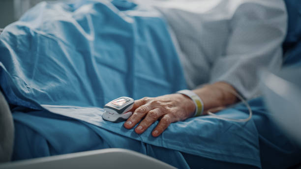 병원 병동: 손가락 심박수 모니터 / 펄스 산소계가 있는 침대에서 쉬고 있는 노인 여성. 그녀의 깨지기 쉬운 손이 담요위에 놓여 있다. 손에 집중하십시오. - hospital ward recovery human age illness 뉴스 사진 이미지
