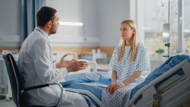 hospital ward: sitting on bed caucasian female patient listens to experienced doctor who explains test results, gives advice, prescribes medicine. woman recovering after successful surgery, sickness - cheerful doctor prescribes professional occupation imagens e fotografias de stock
