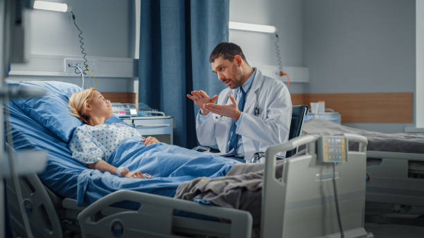 병원 병동: 친절한 의사가 침대에서 쉬고 있는 웃는 젊은 여성과 이야기하고, 병이 끝난 후 완전히 회복됩니다. 의사는 태블릿 컴퓨터를 사용, 검진을 수행, 치료 조언을 제공합니다, 건강 권장 � - hospital ward recovery human age illness 뉴스 사진 이미지