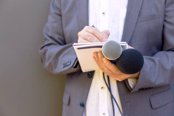 jornalista em evento de mídia ou conferência de imprensa, segurando microfone, escrevendo notas. conceito de jornalismo de radiodifusão. - newspaper the media business new - fotografias e filmes do acervo