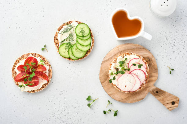 trois pains croustillants au sarrasin sans gluten avec fromage à la crème, radis, tomate, concombre et microgreen pour un petit déjeuner sain sur papier parchemin sur fond de pierre. concept végétalien et alimentation saine. - freedom sandwich bread food photos et images de collection