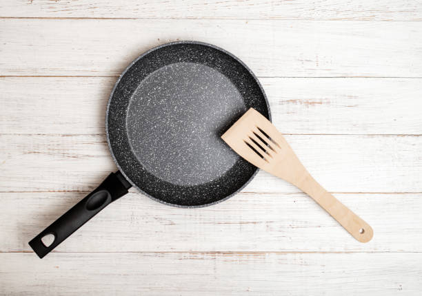 Frying pan with non-stick ceramic coating and spatula on a white wooden background. Cooking without sticking or oil.