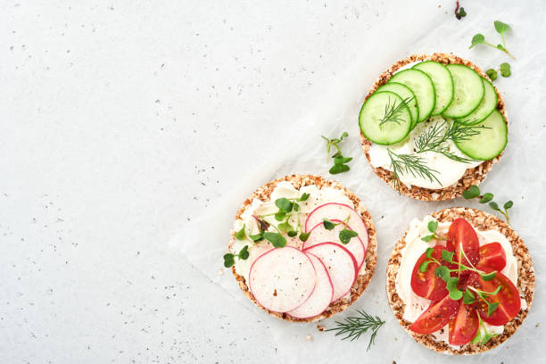 tres crujientes pan de trigo sarraceno sin gluten con queso crema, rábano, tomate, pepino y microvegetal para un desayuno saludable sobre papel pergamino sobre fondo de piedra. concepto vegano y alimentación saludable. - radish vegetable portion circle fotografías e imágenes de stock