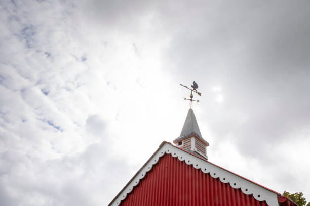 istock Weather vane on a red roof, with dramatic sky, viewed from a low angle with copy space 1321702468