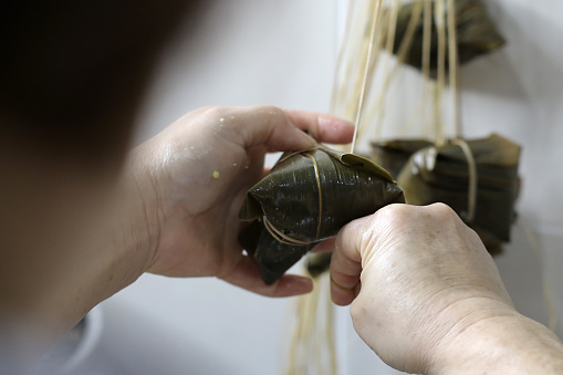 An Asian woman is wrapping zongzi (Chinese rice dumpling) at home.