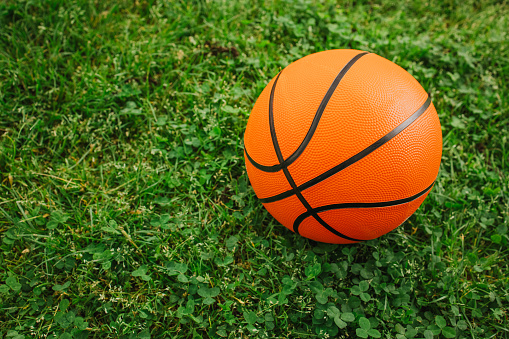 Basketball ball on a fresh green grass. Outdoor kids playground.