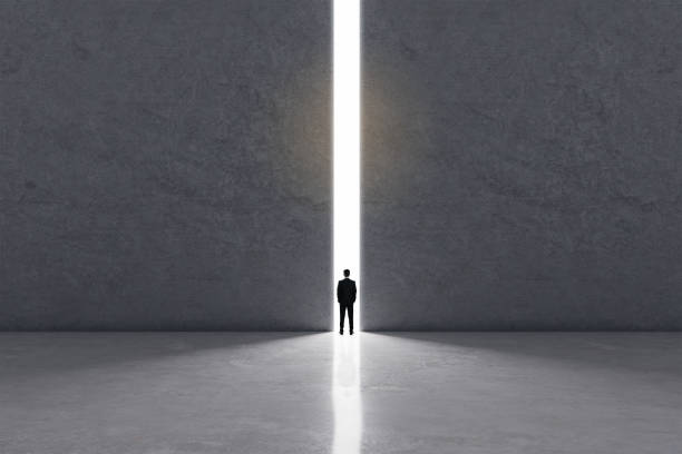 istock Think outside the box concept with businessman back view stays standing in the lighting doorway between big concrete walls. 1321709766