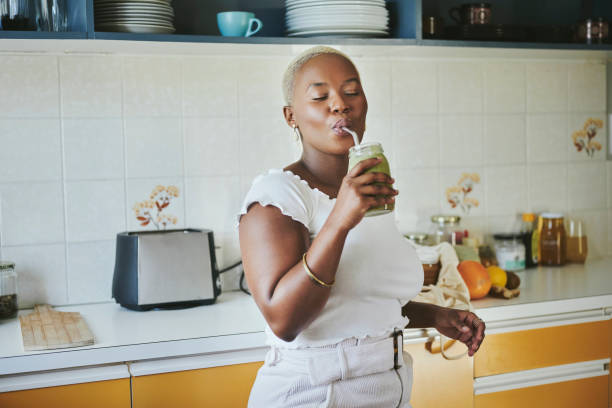 joven africana disfrutando de un batido usando una pajita de metal - batido de frutas fotografías e imágenes de stock