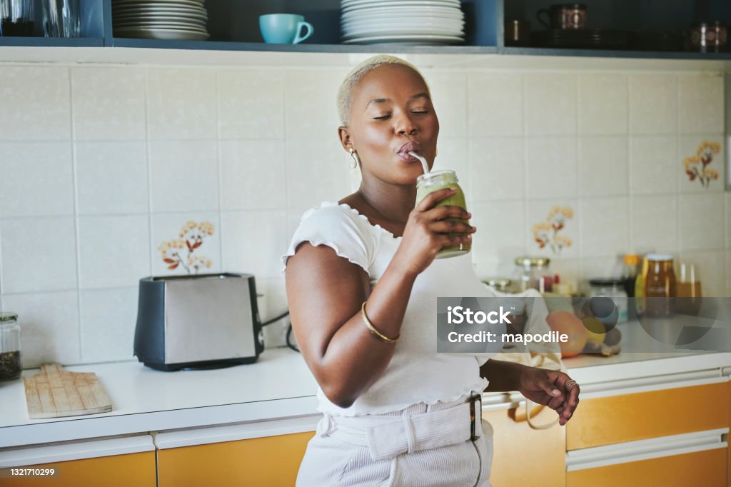 Young African woman enjoying a smoothie using a metal straw Young African woman standing with her eyes closed in her kitchen at home and drinking an organic smoothie with a reusable straw Smoothie Stock Photo