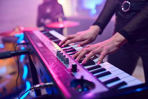 Hands of young woman touching keys of synthesizer during repetition