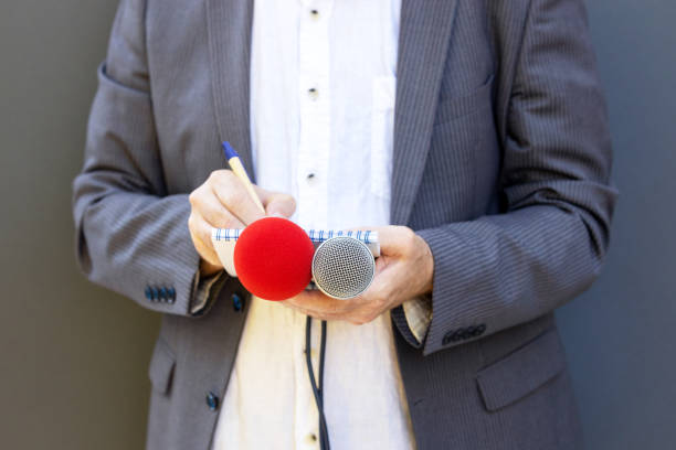 istock Reporter at media event or news conference, holding microphone, writing notes. Broadcast journalism concept. 1321713396
