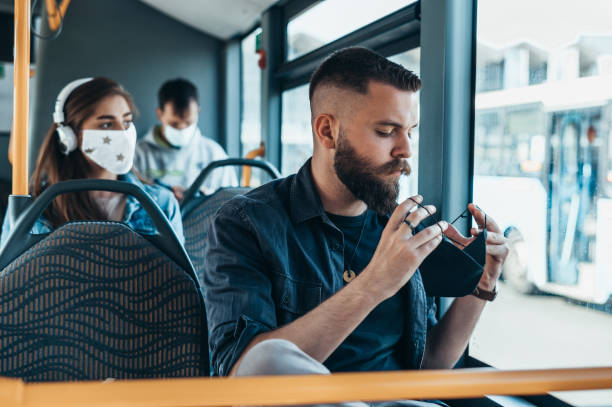 young man wearing protective mask while riding a bus - bus riding public transportation businessman imagens e fotografias de stock
