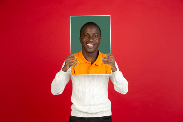 Young african man holding his portrait isolated over red studio background with copyspace for ad.