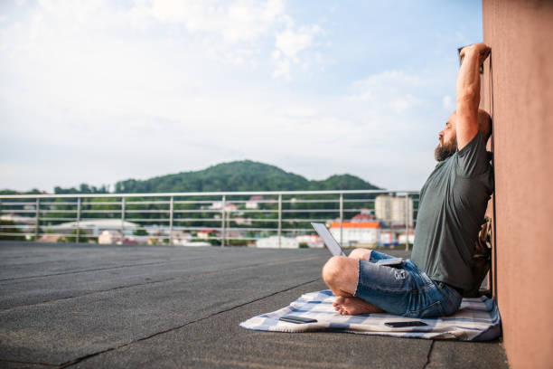 istock Man with laptop makes relaxation exercise at the rooftop 1321723536