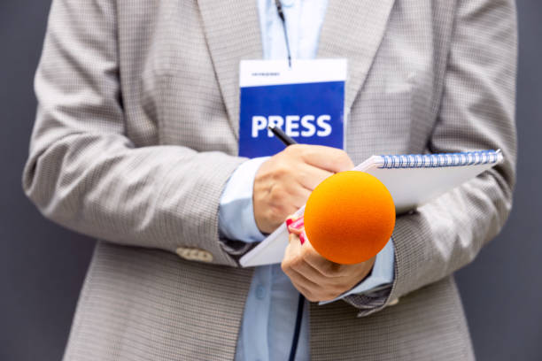 istock Female reporter at press conference or media event, writing notes, holding microphone. Broadcast journalism concept. 1321723692